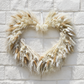 Heart-shaped dried pampas grass wreath in beige and white hanging on a white brick wall.