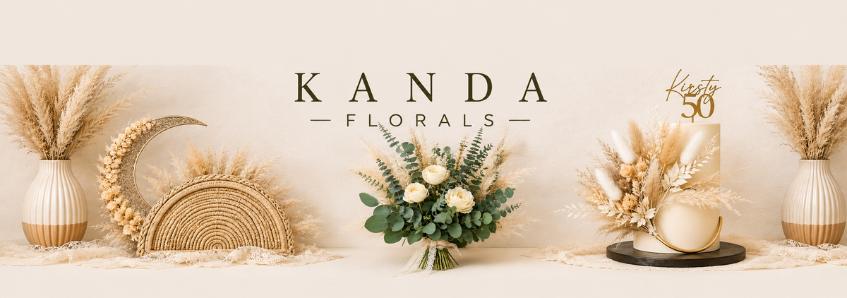 A decorative banner with the text 'KANDA FLORALS' centered on a warm cream background, flanked by pampas grass in vases, a woven basket, a floral arrangement, and a gold birthday cake topper.