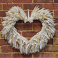 A heart-shaped dried pampas grass wreath hanging on a red brick wall.