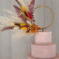 A pampas grass wreath with a mixture of dried flowers attached to a cake.