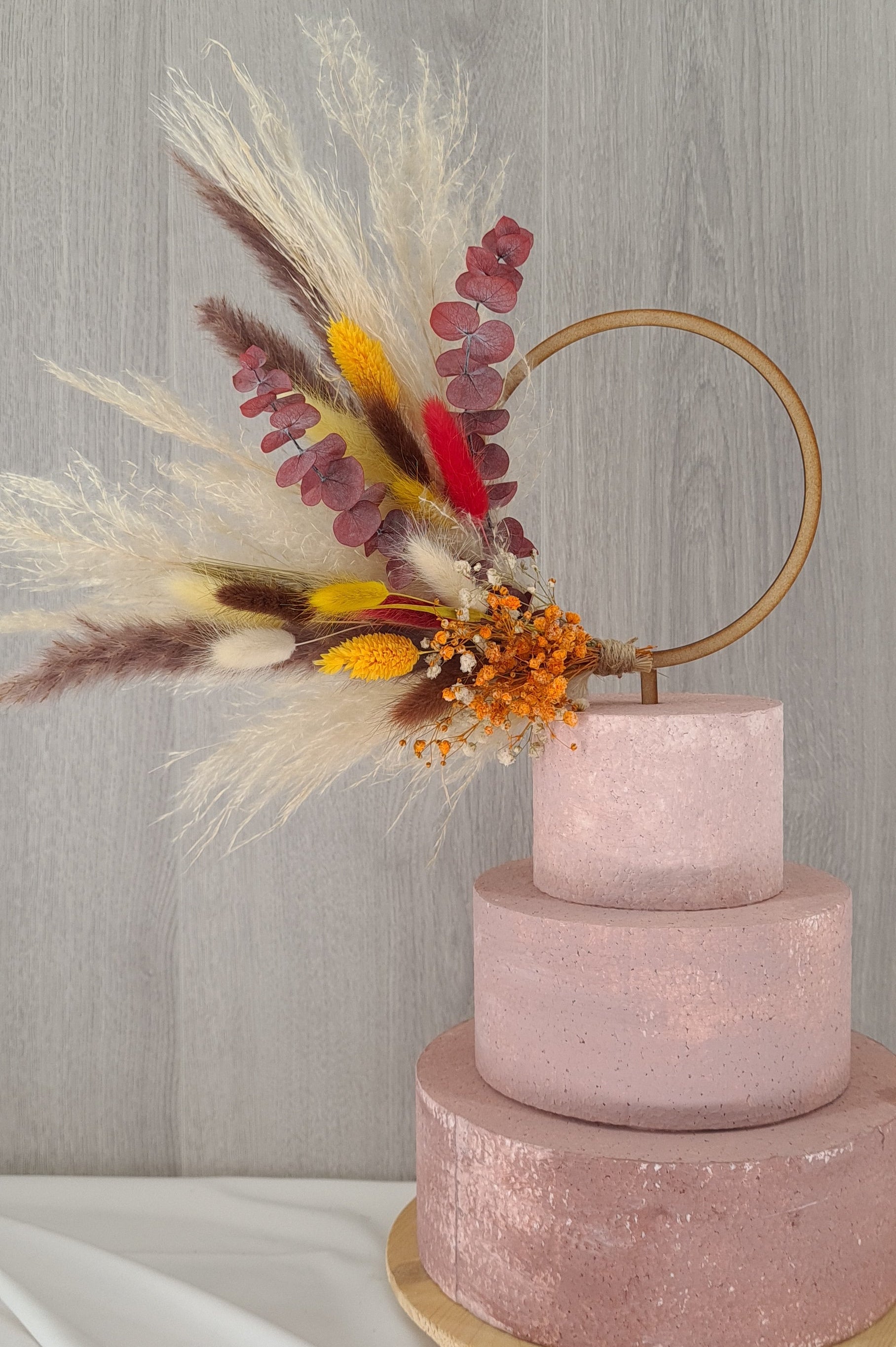 A pampas grass wreath with a mixture of dried flowers attached to a cake.